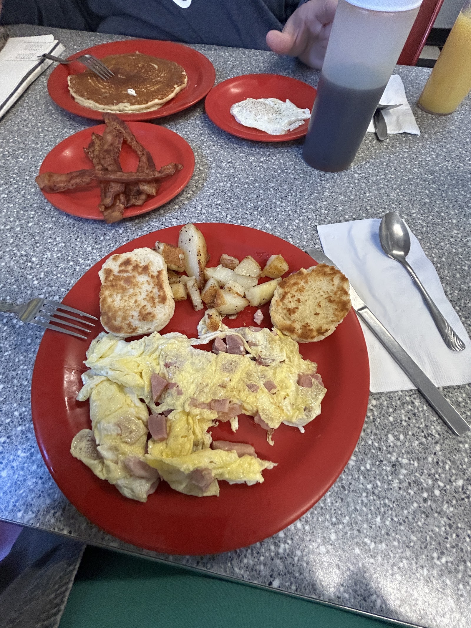 Pancakes, bacon, eggs, an omelette and English muffins across a table of red plates.